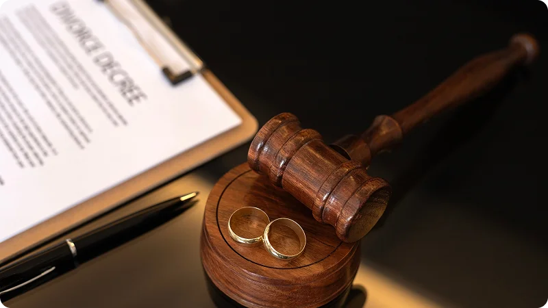 A wooden gavel, two wedding rings, and a pen resting on a "DIVORCE DECREE" document.