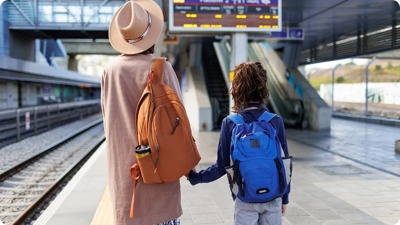 Woman and child with backpacks waiting on a train platform.