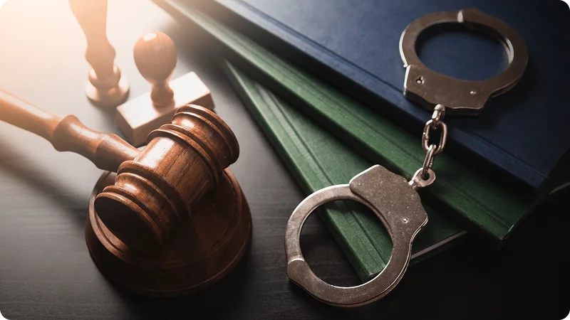 A wooden gavel and handcuffs resting on several law books.