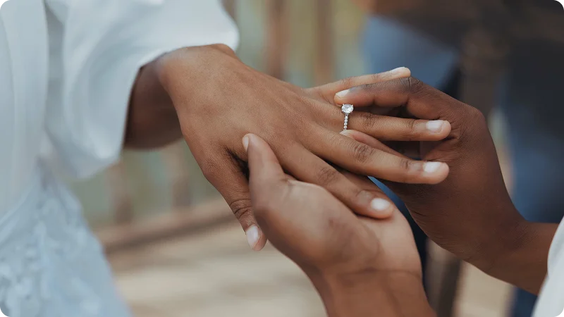 A close-up of one person sliding a diamond engagement ring onto another person's finger.