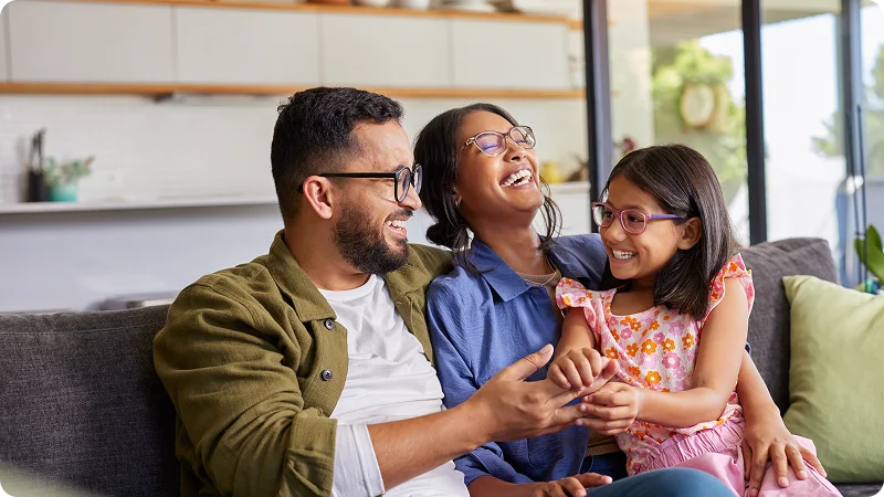 Happy family of three laughing together on a couch.