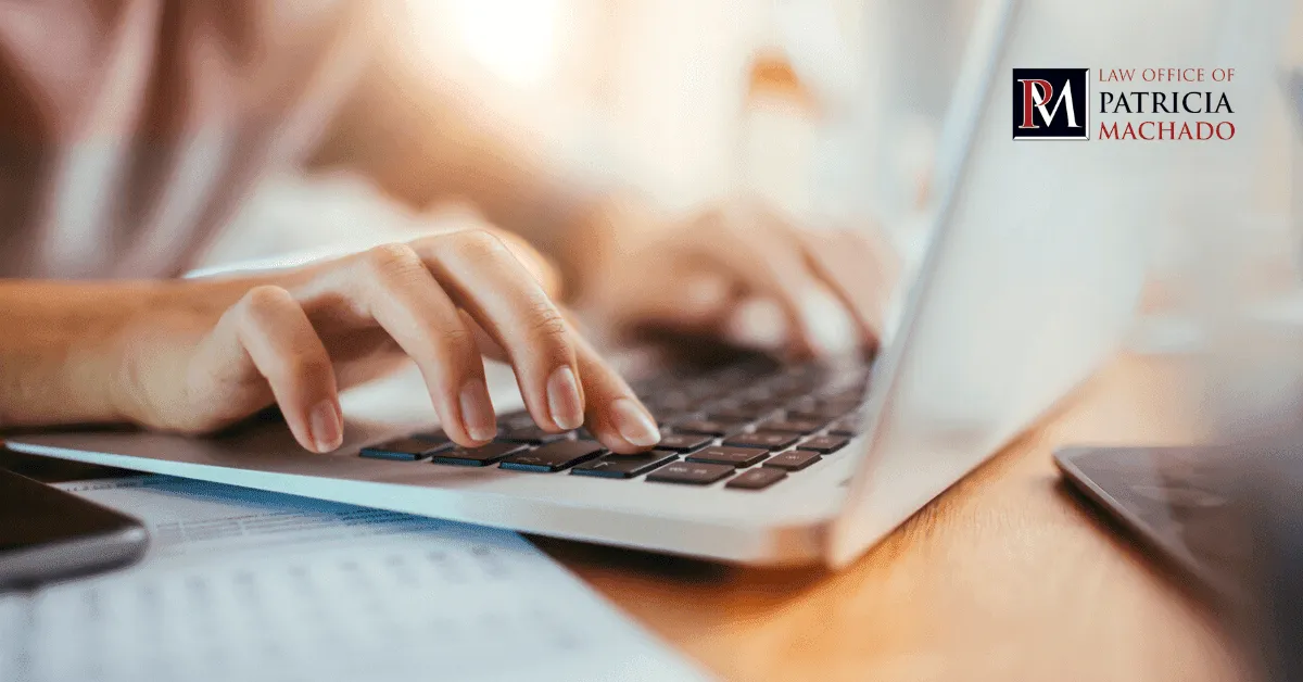 A close-up of hands typing on a laptop keyboard over documents on a desk.