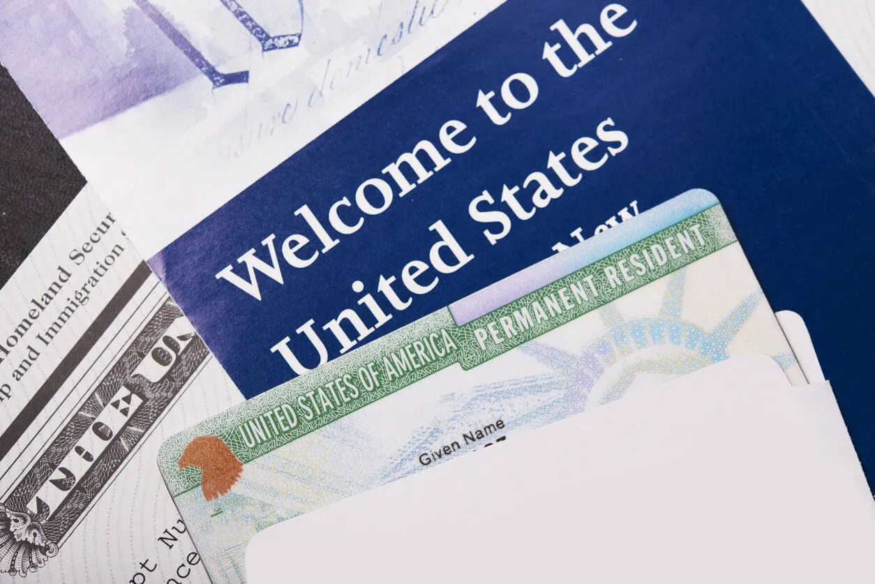 A close-up of a U.S. Permanent Resident Card (Green Card) tucked into an envelope next to a booklet.