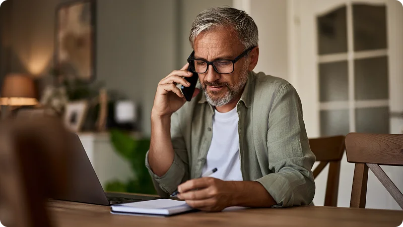 Man talking on a phone while looking at a notebook.