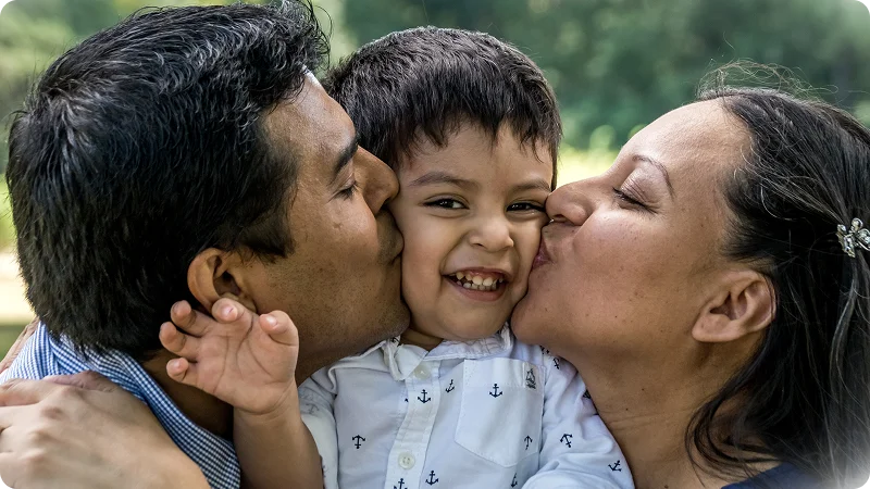 Two parents kissing a smiling child on the cheeks.