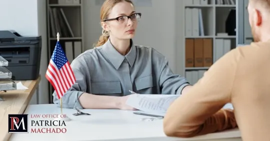 A legal professional with glasses sits at a desk with a small U.S. flag and consults with a client.