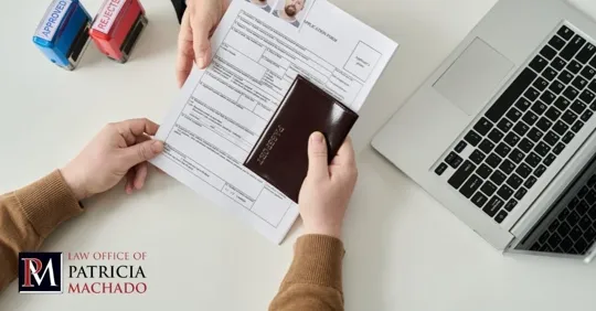 Overhead view of hands holding a passport and an application form on a desk next to a laptop.