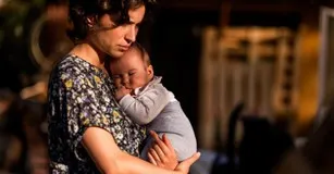 A woman in a floral shirt holds a sleeping baby close to her chest.