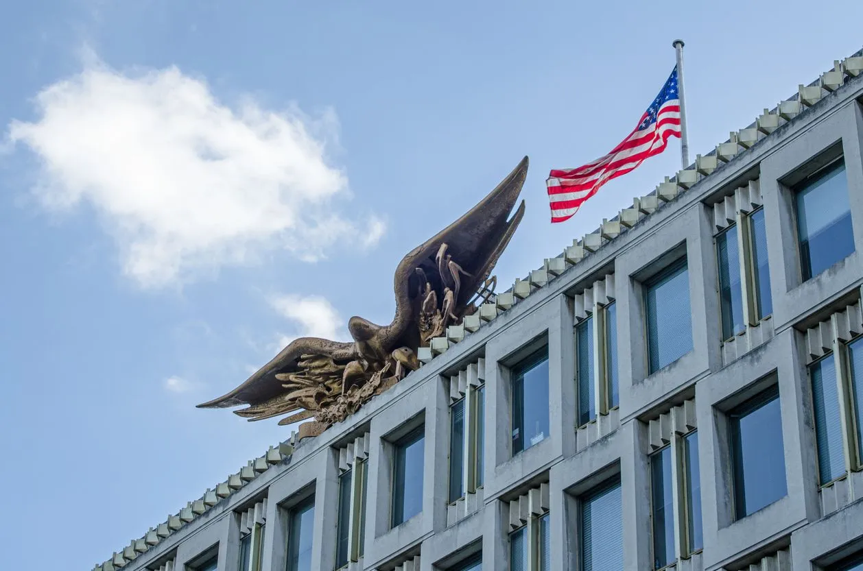 Low-angle view of a concrete building with a large bronze eagle sculpture and an American flag.