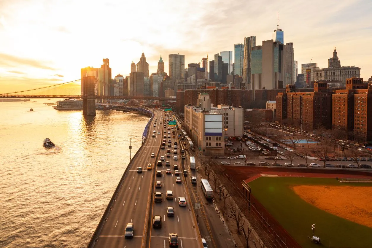 A sunset view of the New York City skyline, the Brooklyn Bridge, and heavy traffic.