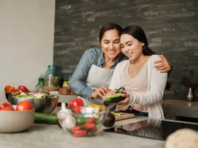 Two women smiling while preparing food together in a kitchen.