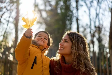 A woman and child smiling while holding a golden leaf up to the sun.