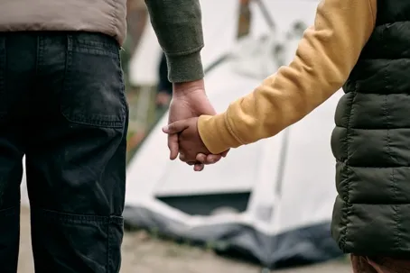 Two people holding hands while standing in front of a white and black tent at a campsite.