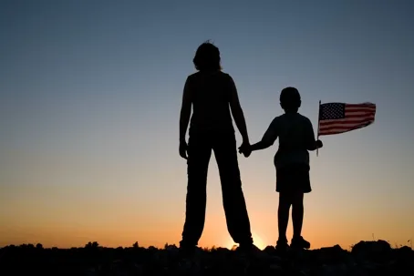 Silhouette of a woman and child holding an American flag at sunset.