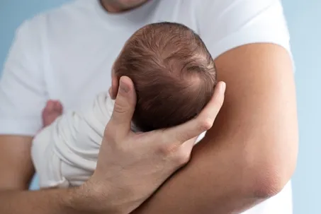 A person in a white t-shirt cradling a newborn baby's head.