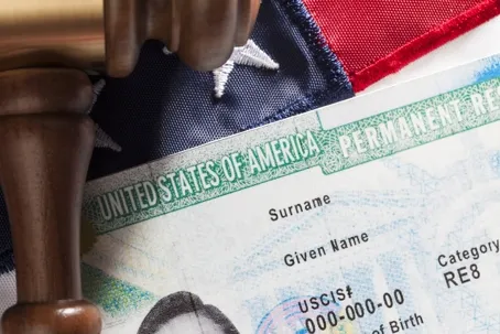 A United States Permanent Resident card (Green Card) resting on a U.S. flag next to a wooden gavel.